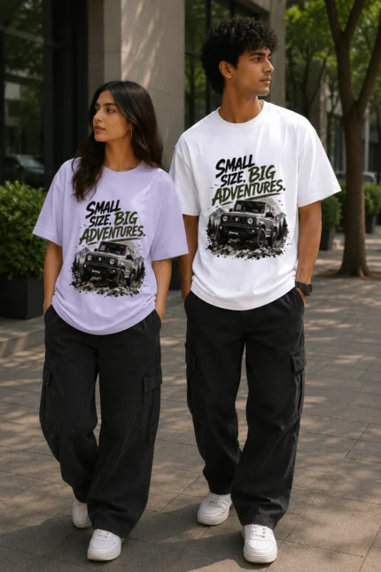 "Male and female models wearing oversized graphic T-shirts with the 'Small Size. Big Adventures.' off-road vehicle print. The woman wears a lavender oversized tee, while the man wears a white oversized tee, styled with black cargo pants in a modern urban outdoor setting."