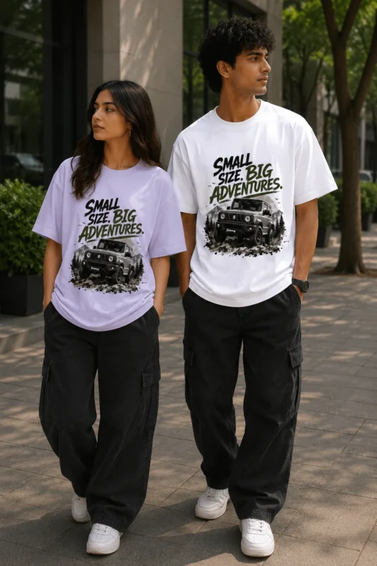 "Male and female models wearing oversized graphic T-shirts with the 'Small Size. Big Adventures.' off-road vehicle print. The woman wears a lavender oversized tee, while the man wears a white oversized tee, styled with black cargo pants in a modern urban outdoor setting."